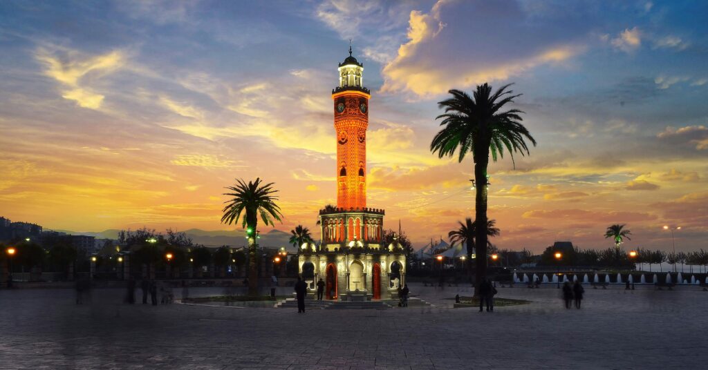 Stunning view of Izmir's iconic clock tower glowing at sunset, surrounded by palm trees.