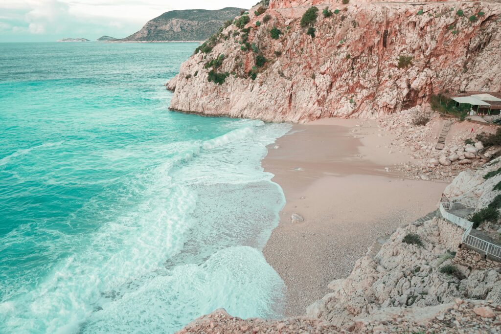 Serene view of sandy beach with waves crashing against rocky cliffs in Antalya, Türkiye.