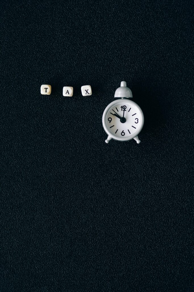 Miniature clock and word tax on black background symbolizing tax season deadlines.